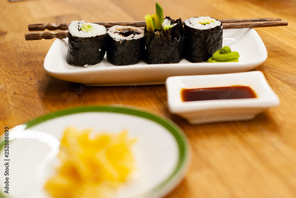 自制素食寿司卷，里面放着鳄梨，放在木桌上的一个小盘子里，放着酱油，哇
