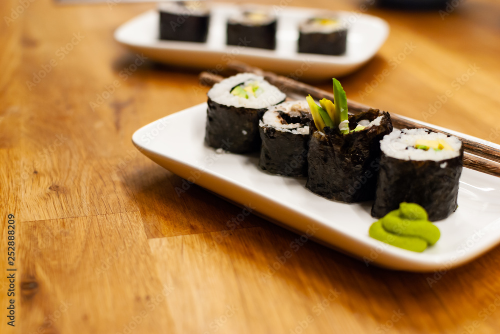 Homemade vegan Sushi rolls filled with avocado on a small plate on a wooden table with soy sauce, wa