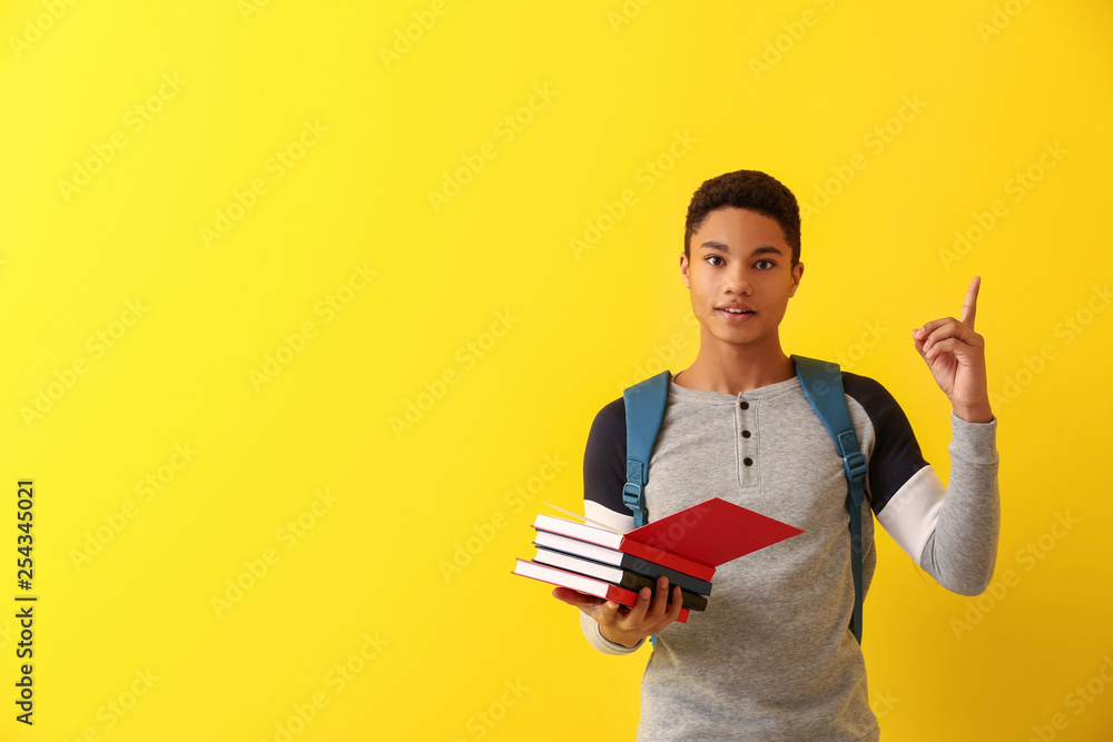 African-American schoolboy with books and raised index finger on color background