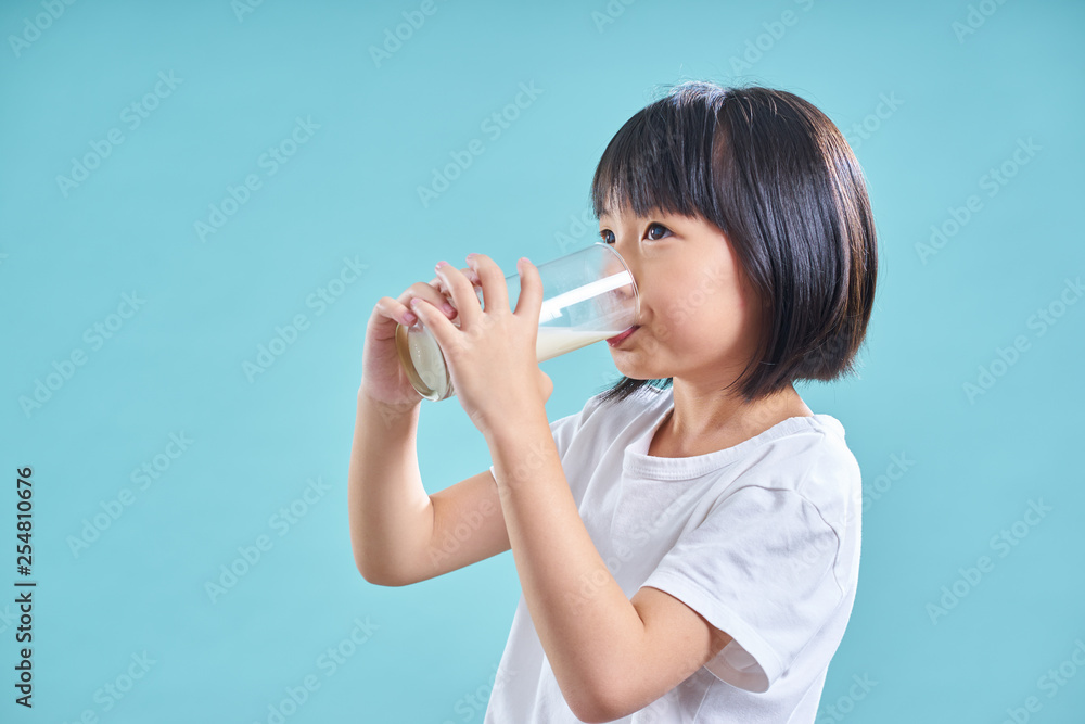 Asian little girl enjoy to drinking glass of milk isolated on light blue background  .