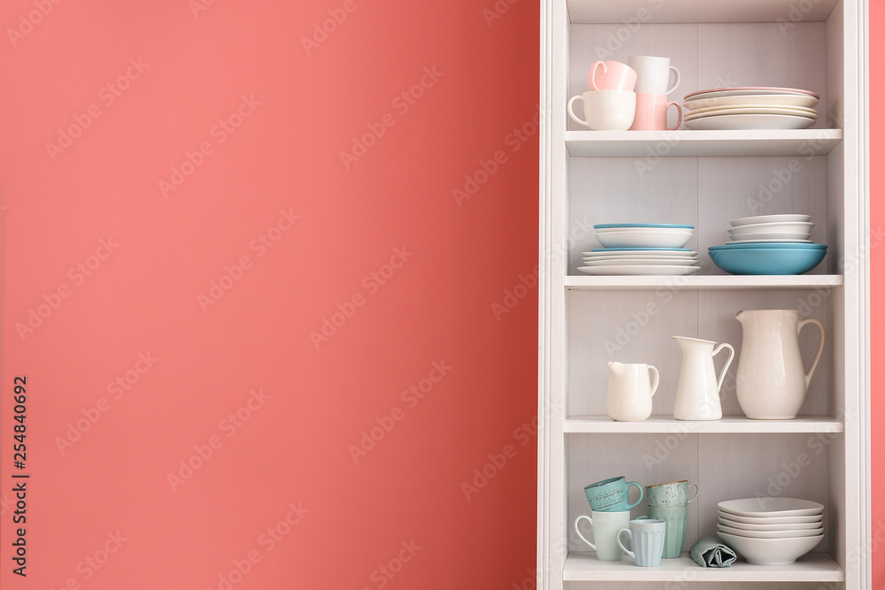 Set of clean dishes on shelves near color wall