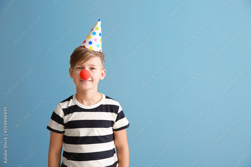Little boy with clown nose and party hat on color background. April fools day celebration