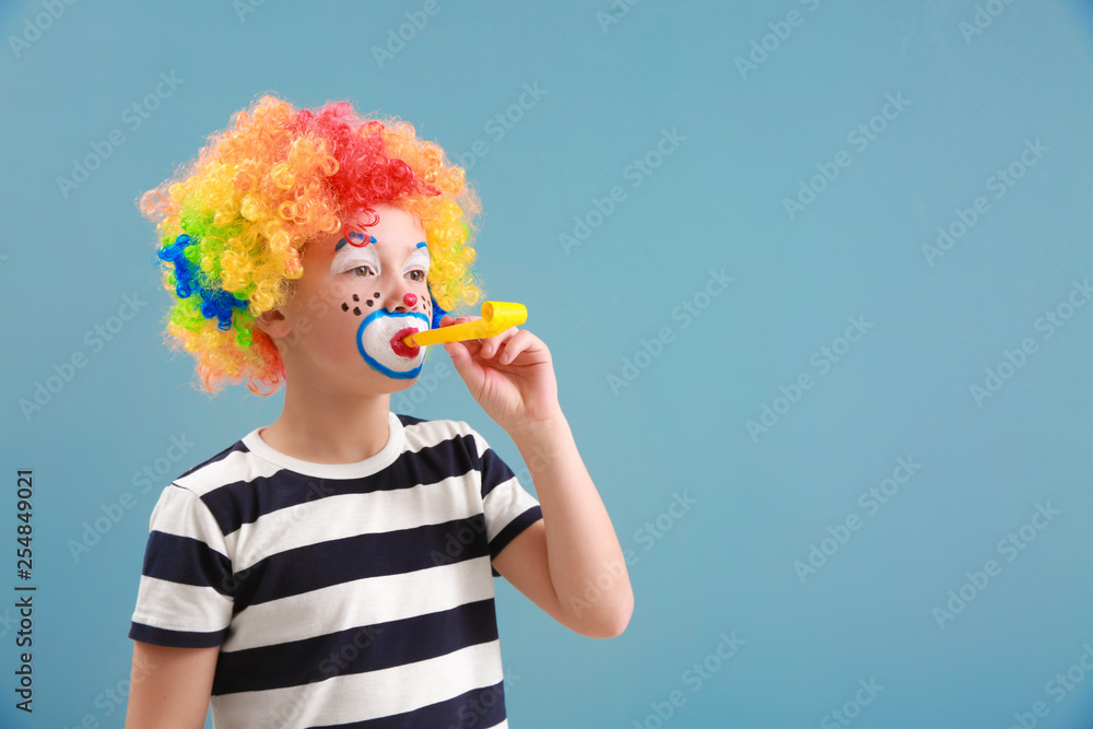 Cute little boy with clown makeup and party whistle on color background. April fools day celebratio