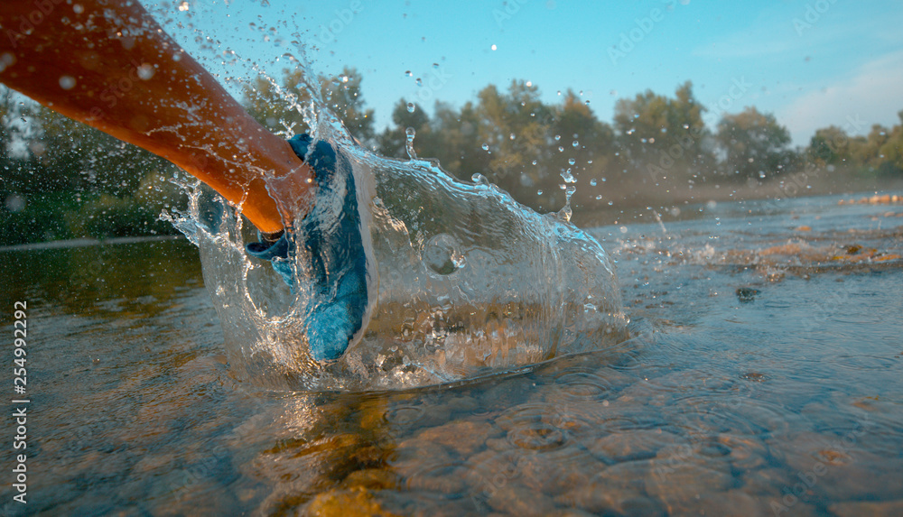 低角度：一个无法辨认的人在河里奔跑，泼洒着令人耳目一新的水。