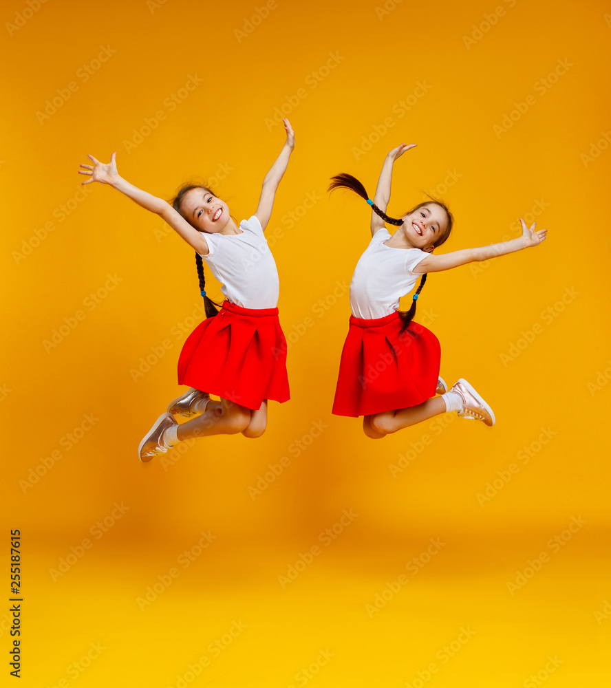有趣的孩子女孩双胞胎在黄色背景上跳跃。