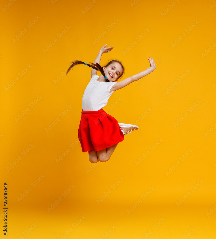 有趣的小女孩在黄色背景上跳跃。