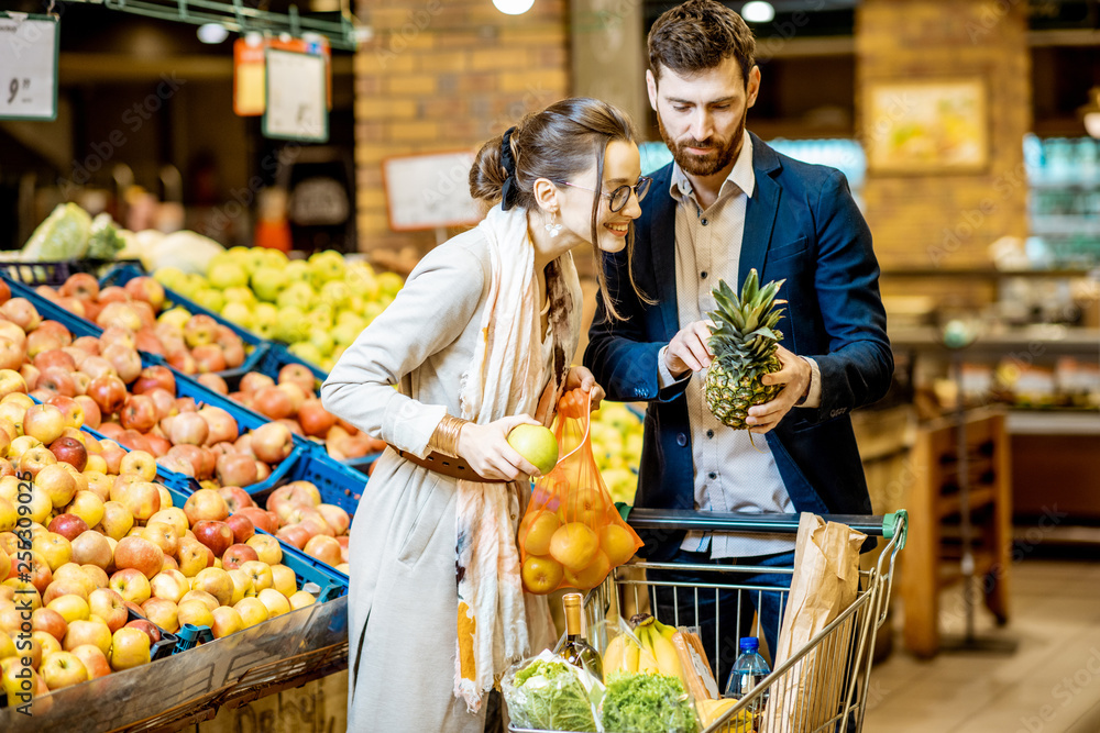 年轻幸福的一对夫妇站在购物车旁购买新鲜水果和蔬菜