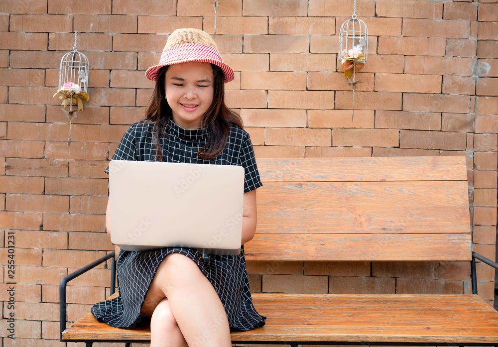Young woman using laptop computer on bench against brick wall.