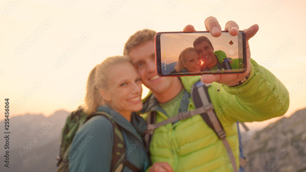 CLOSE UP: Cheerful man holding his smartphone as he takes selfie with girlfriend