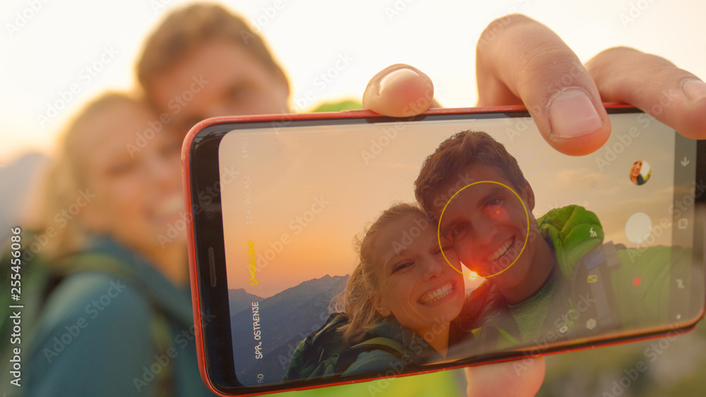 MACRO：一对微笑的年轻徒步旅行者在日出时在山顶自拍。