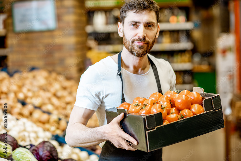 一位英俊的店员或农民的肖像，手里拿着一个盒子，里面装着新鲜的西红柿