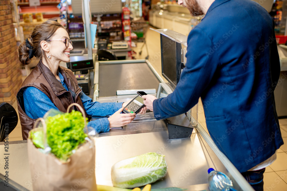一名男子用信用卡在收银台购物，超市收银员兴高采烈