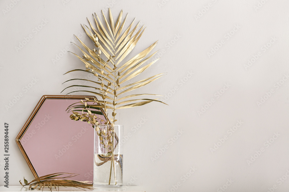 白色墙壁附近桌子上的金色热带树叶和镜子