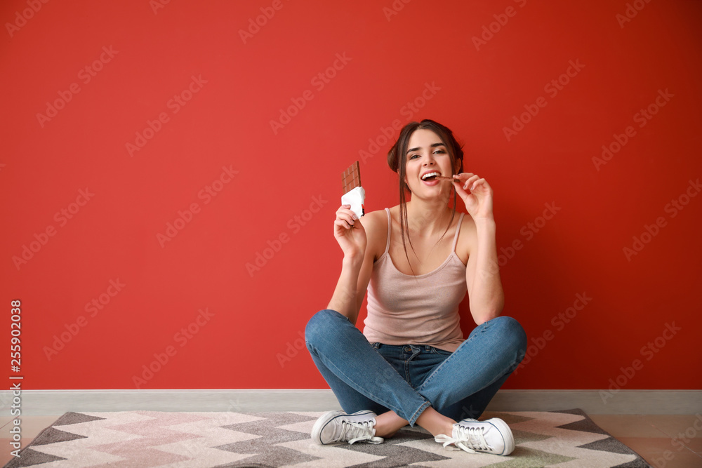 漂亮的年轻女人，拿着美味的巧克力坐在靠近彩色墙的地板上