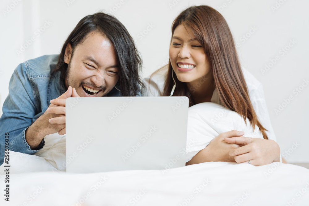一对亚洲年轻夫妇在床上用笔记本电脑看电影