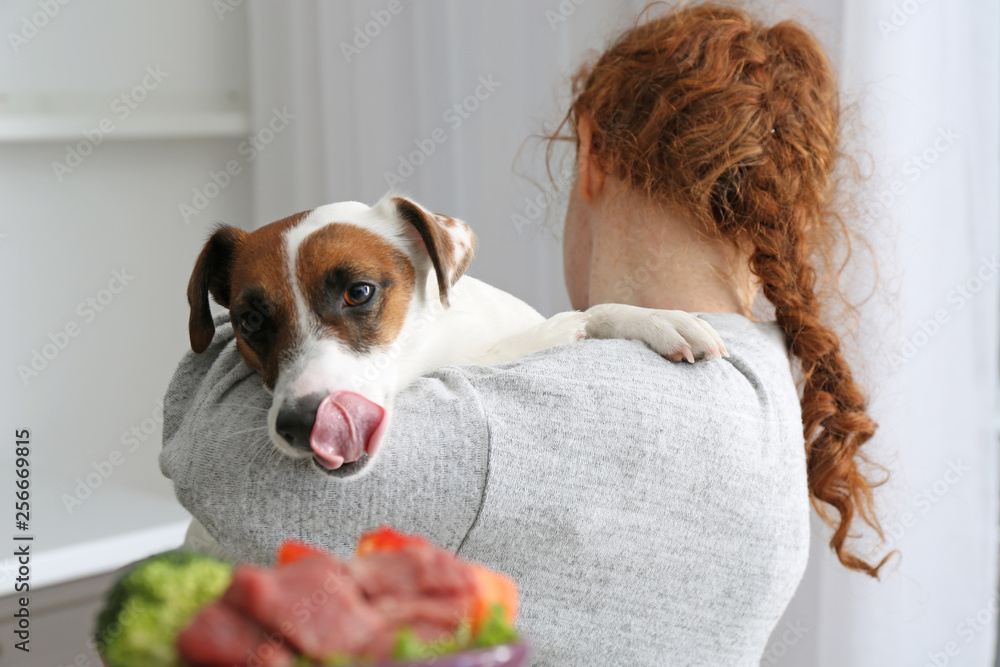Woman holding cute funny dog looking at bowl with food