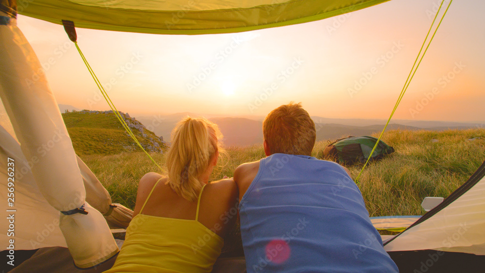 特写：一对年轻的徒步旅行者夫妇躺在帐篷里观察日落。