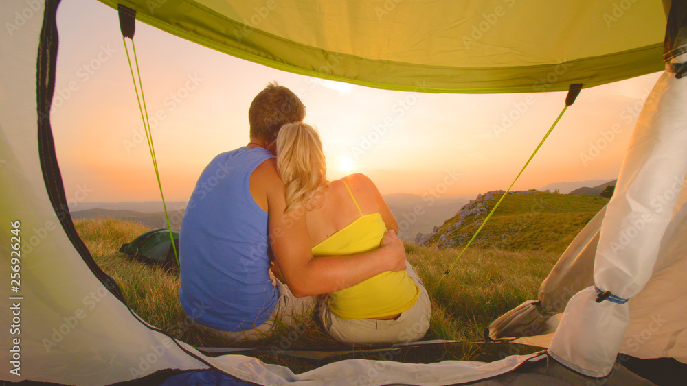 镜头闪耀：年轻的徒步旅行者拥抱在帐篷前观看日落。