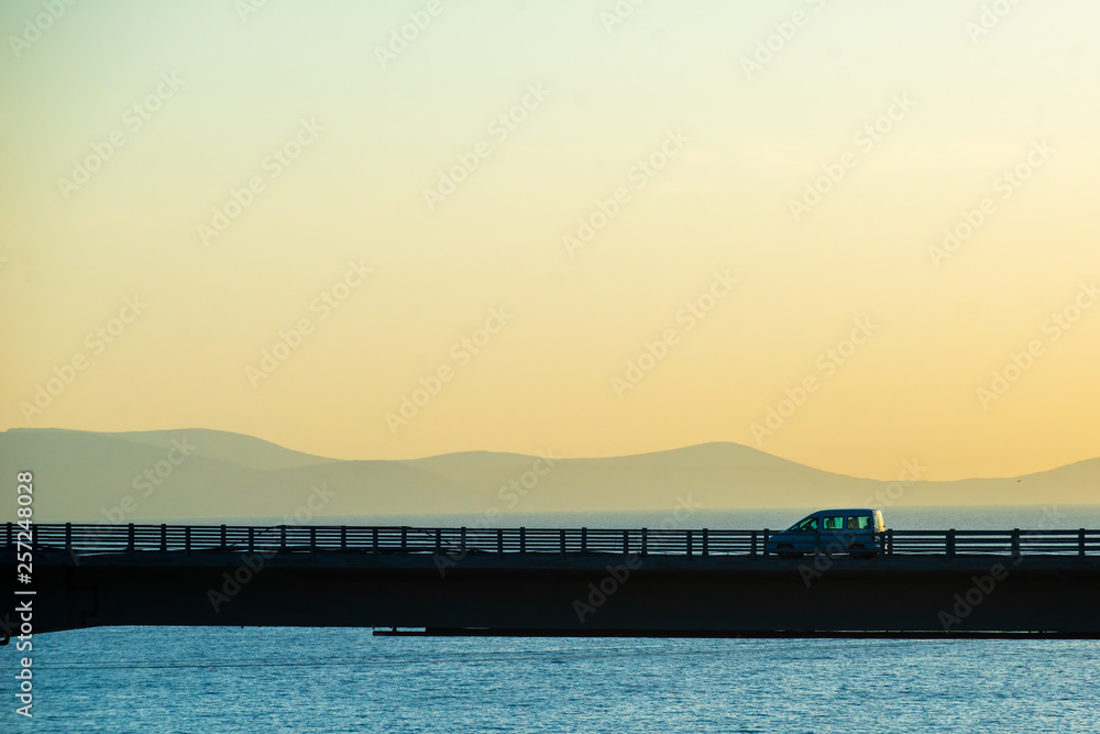 Cars on the highway bridge during the dawn against the backdrop of mountains and the sea