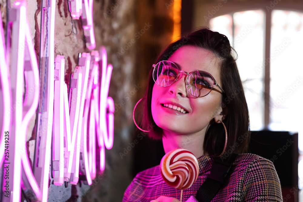 Toned portrait of beautiful young woman near neon lighting on wall