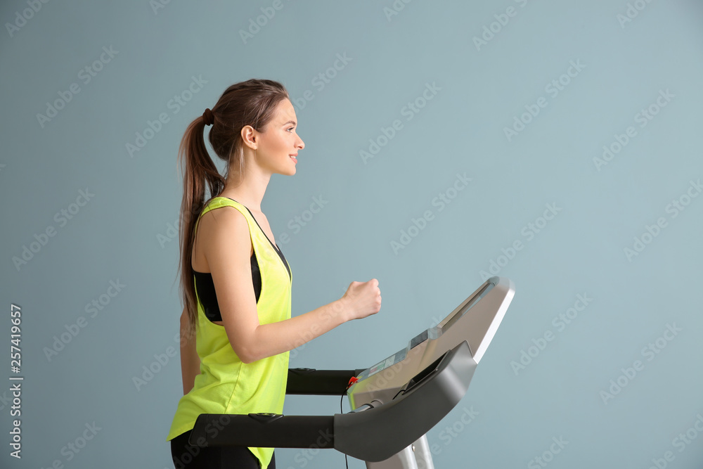 运动型年轻女性在彩色背景下的跑步机上训练