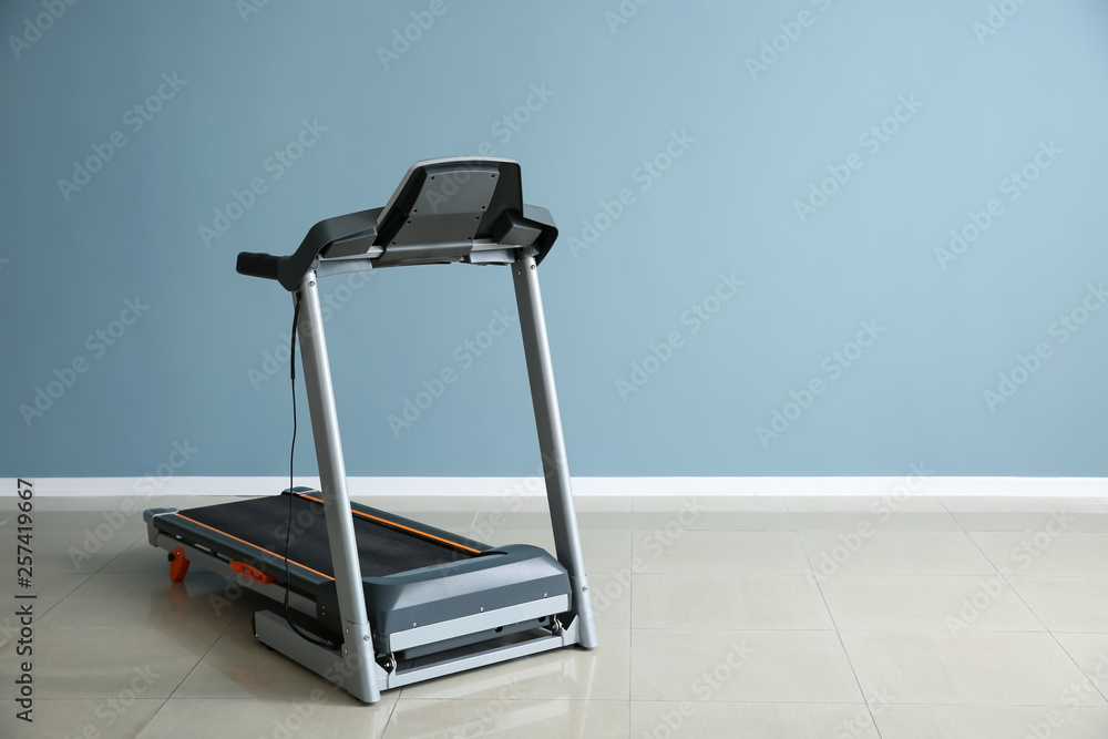 Modern treadmill near color wall in gym