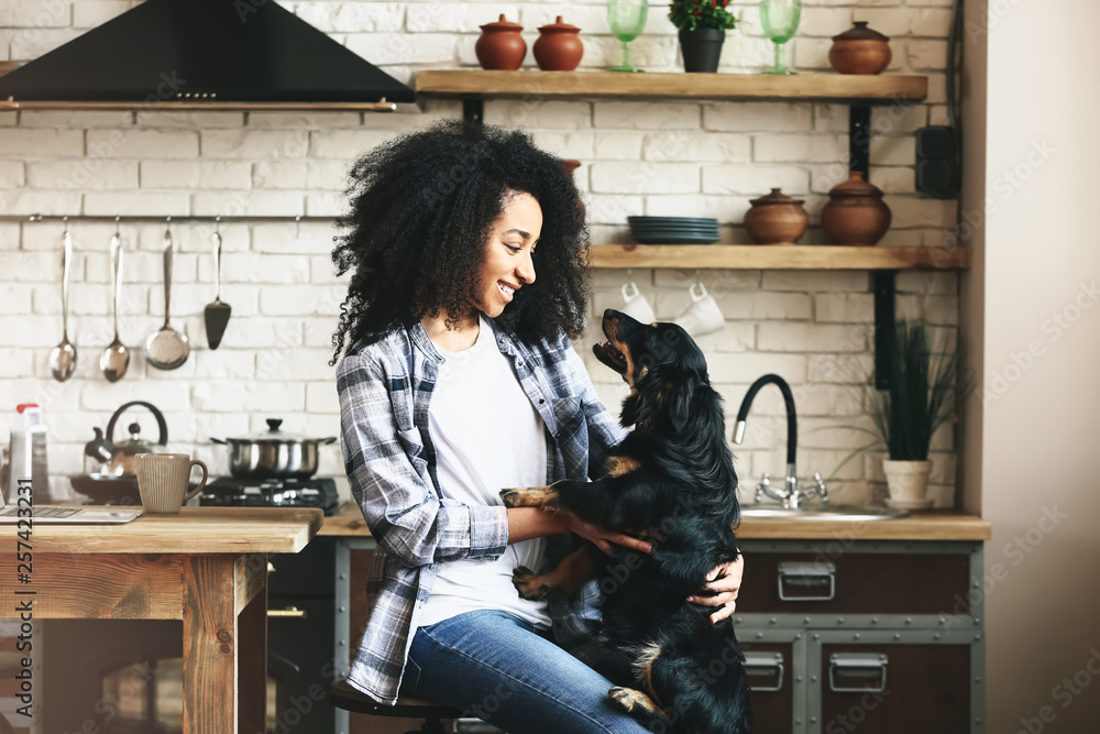 African-American woman with cute funny dog in kitchen