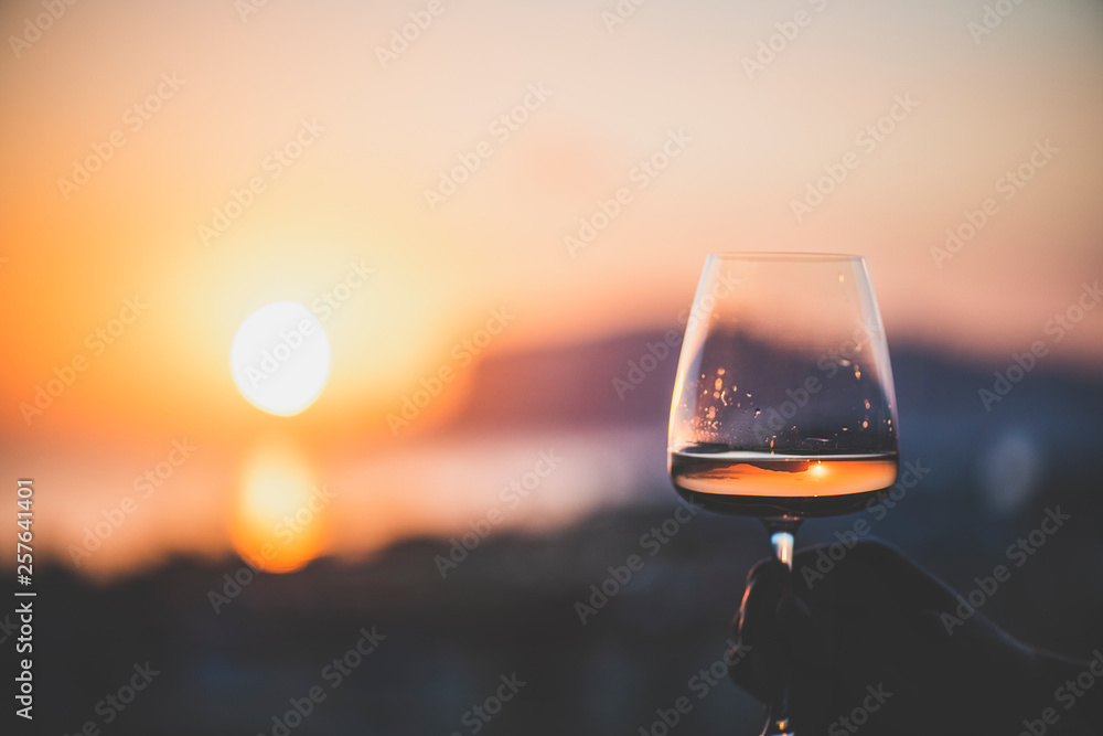男人手拿一杯玫瑰酒，背景是大海和美丽的日落，特写，霍尔