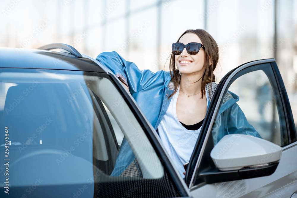 Portrait of a young and happy woman standing near the modern car outdoors