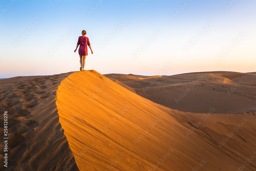 日落时分，女孩穿着连衣裙走在干旱沙漠的沙丘上，撒哈拉的风景或