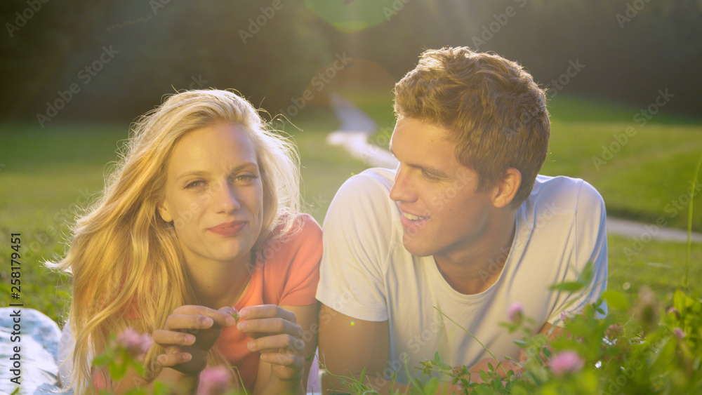 肖像：一对年轻的学生夫妇躺在宁静的草地上打电话回家。