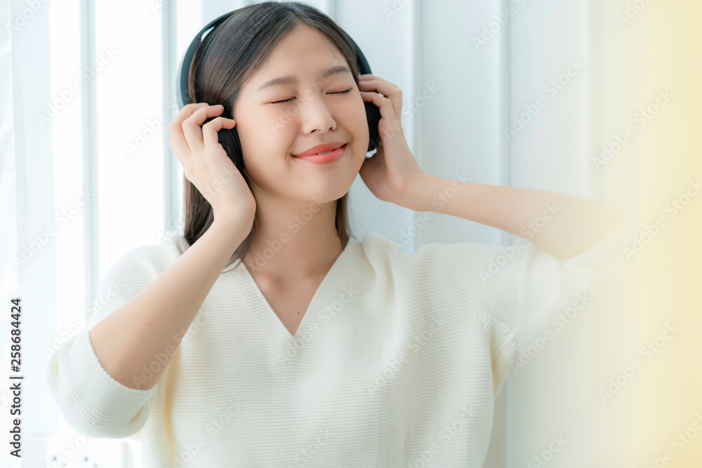 迷人的亚洲美女用耳机享受音乐，幸福快乐，就像肖像一样