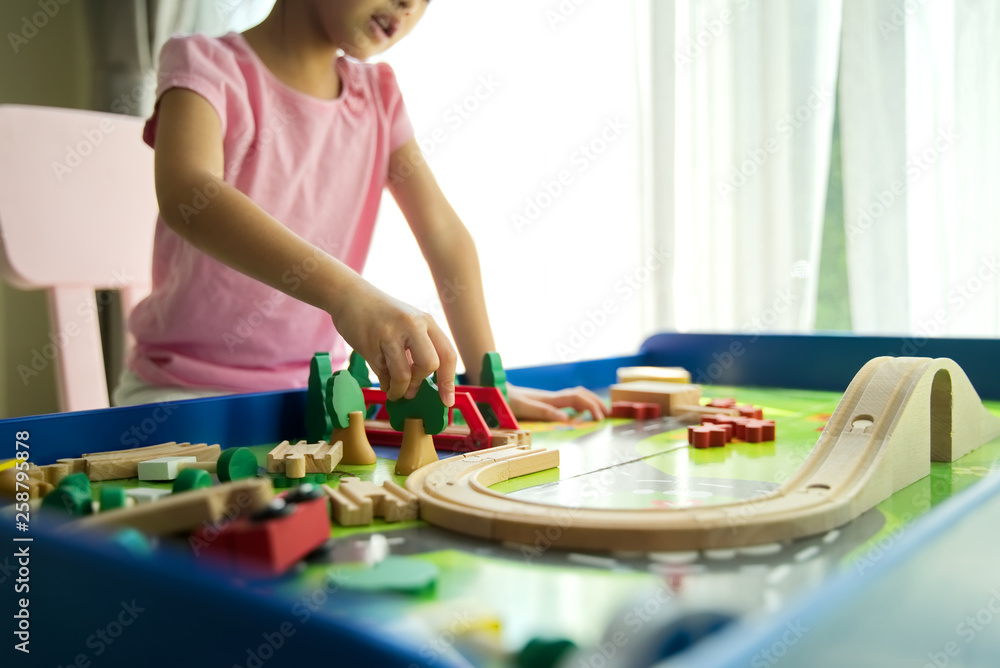 年轻的亚洲小可爱在家里的桌子上玩木制玩具。她正在用广场建造小城市