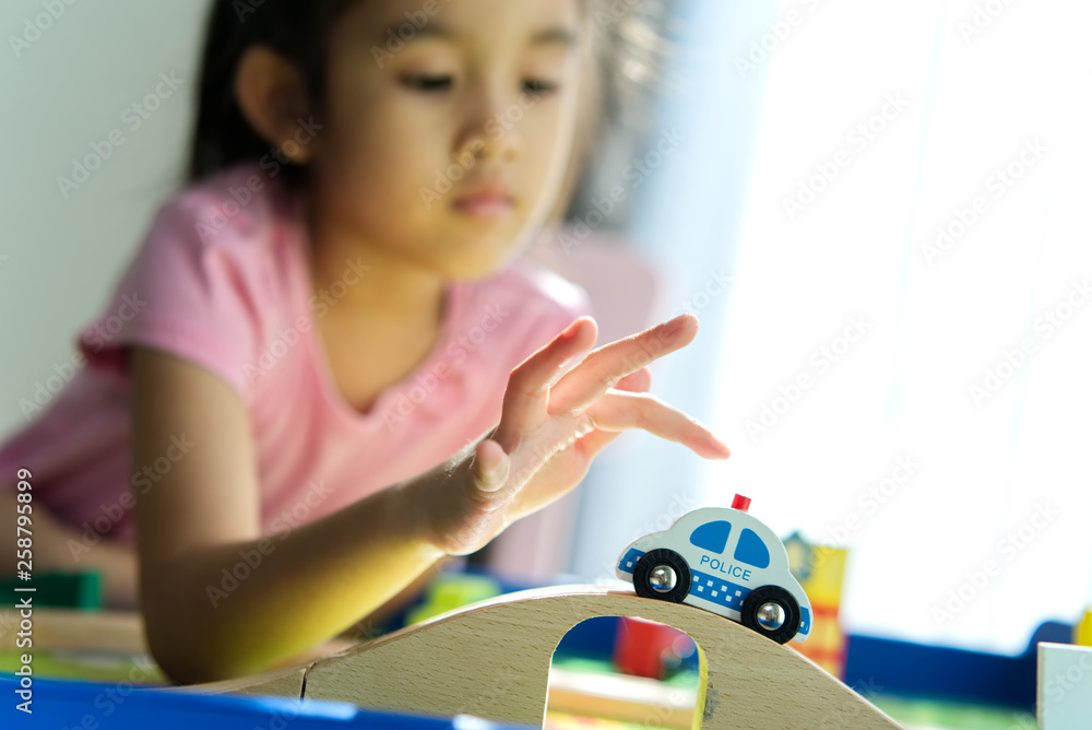 年轻的亚洲小可爱在家的桌子上玩木制玩具。她推着一辆车在路上行驶