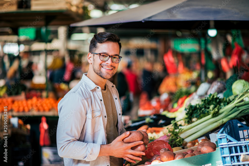 微笑的英俊男子在街头市场买新鲜蔬菜。