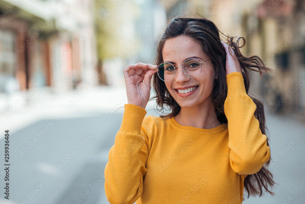 城市里一位戴着眼镜的乐观年轻女性的头像，对着镜头微笑。