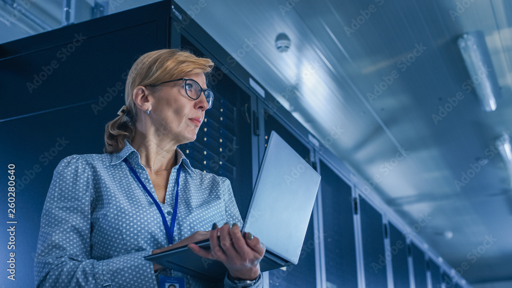 在数据中心：女性IT技术员在笔记本电脑上运行维护程序，控制操作