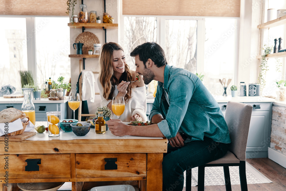 试试看！漂亮的年轻夫妇坐在家里的厨房里享用健康的早餐