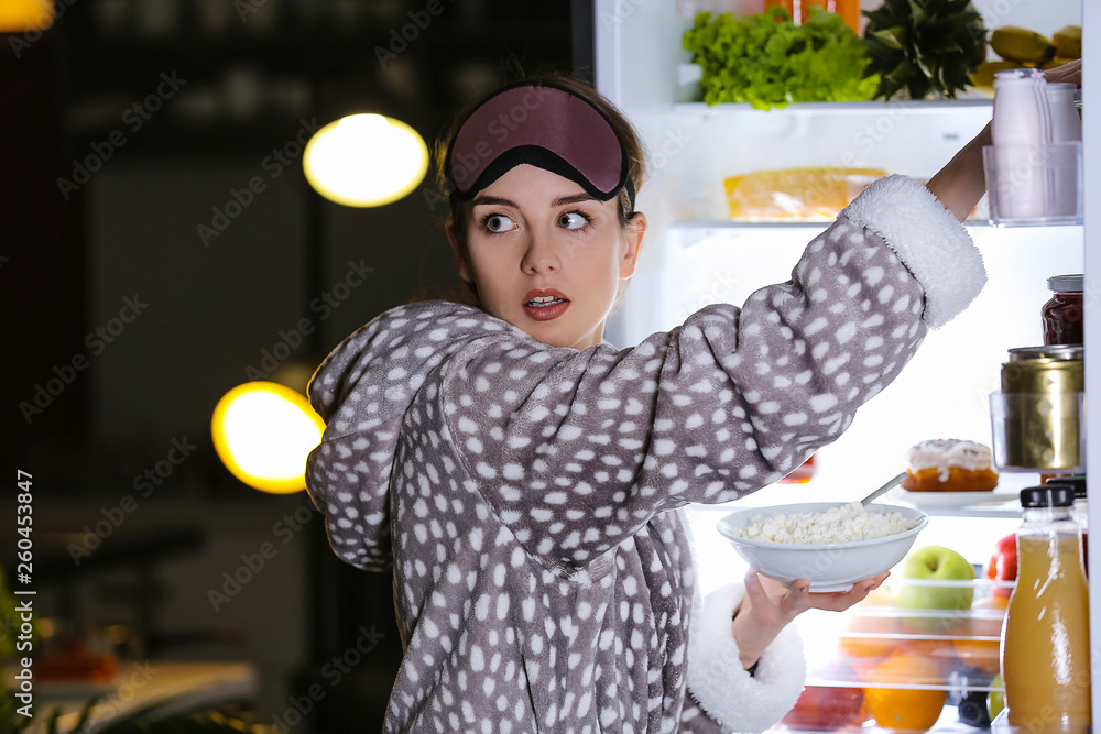 警惕的年轻女子晚上在冰箱里挑选食物