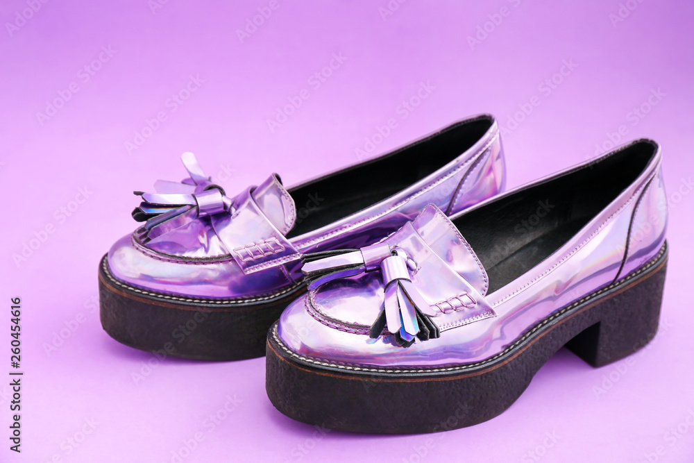 Stylish female shoes from iridescent material on color background