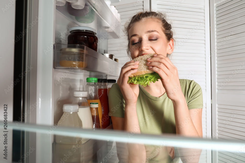 漂亮的年轻女人在冰箱附近吃东西，从里面看