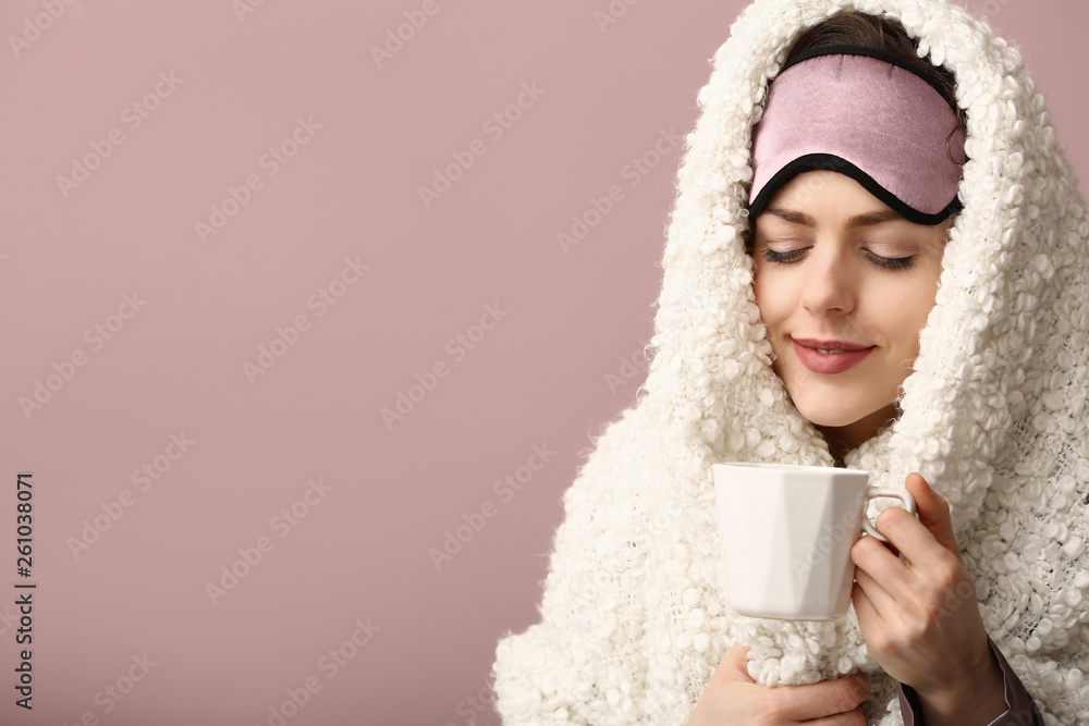 Young woman with sleep mask, cup of coffee and plaid on color background