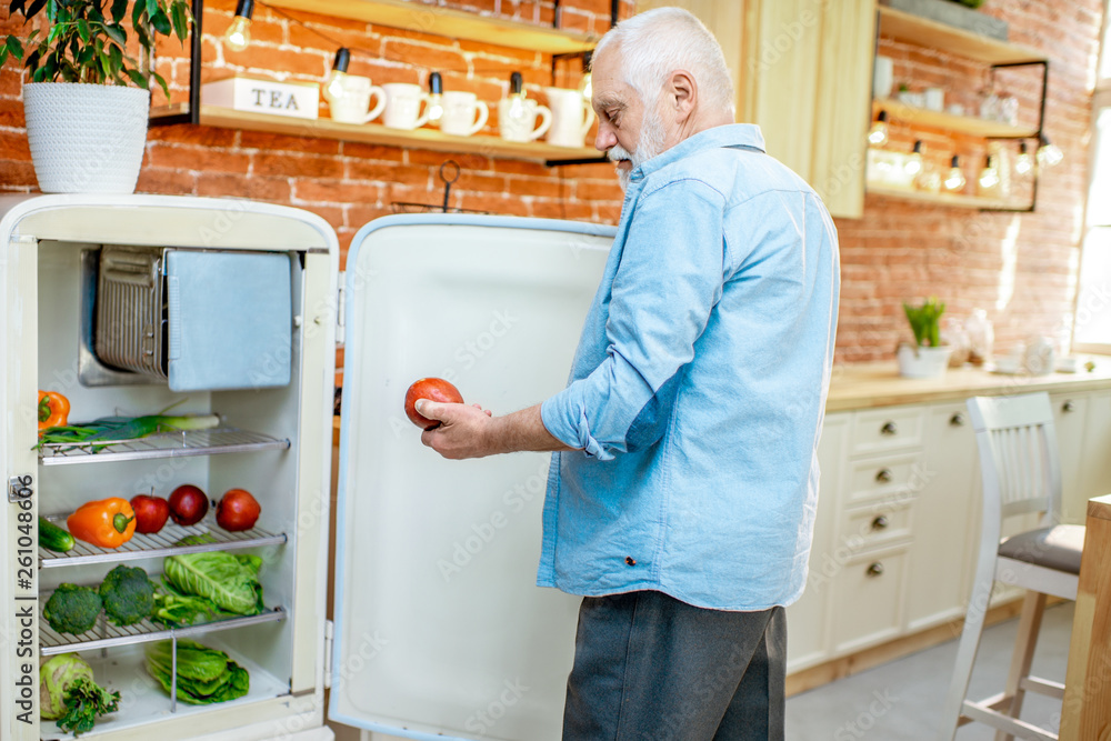老人在家厨房打开装满健康新鲜产品的冰箱