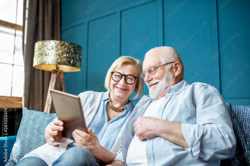 Lovely senior couple dressed casually using digital tablet while sitting together on the comfortable