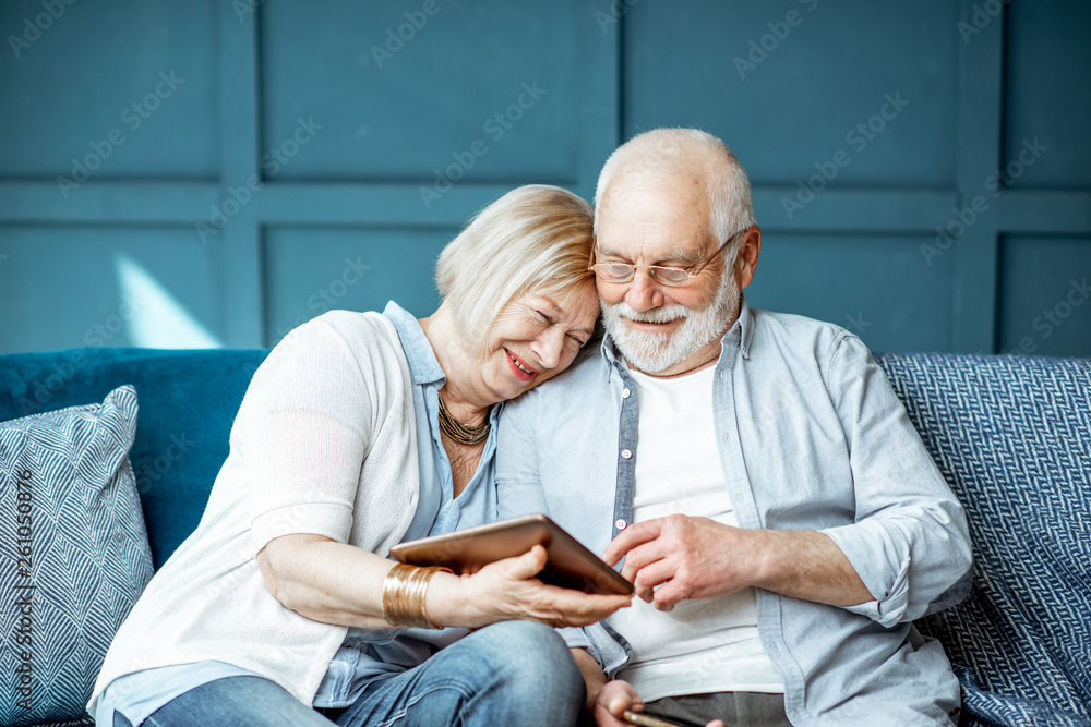 一对可爱的老年夫妇坐在一起，穿着休闲，使用数字平板电脑