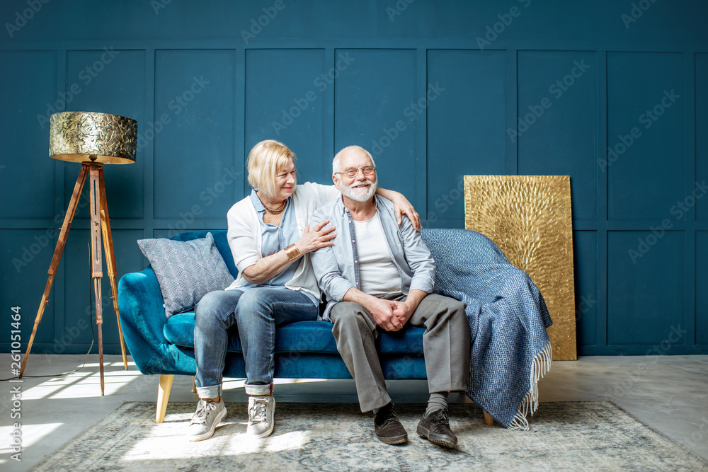 Lovely senior couple sitting together on the couch in the living room at home, wide interior view