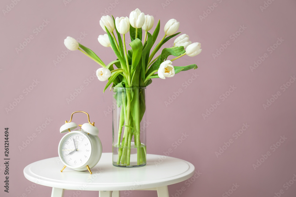 餐桌上摆放着一束新鲜的郁金香花和彩色背景的闹钟