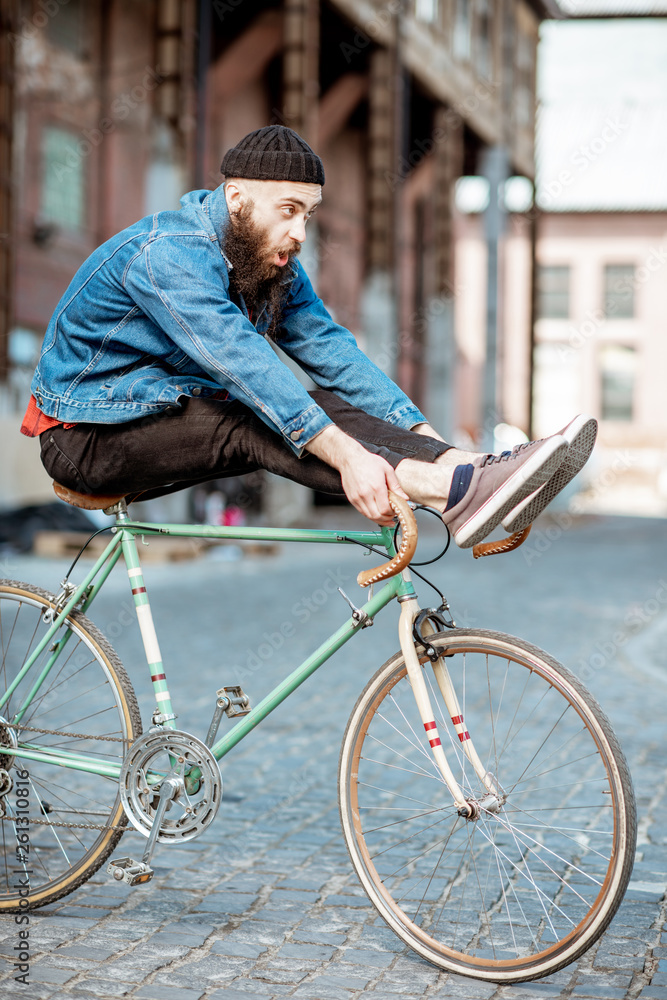 时尚的男人，作为一个疯狂的潮人，在工业城市的户外骑复古自行车，玩得很开心