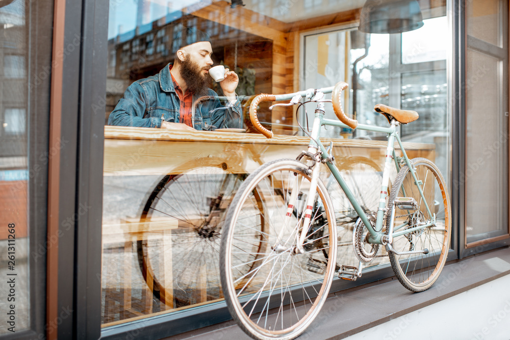 时尚男子骑着复古自行车坐在靠窗的咖啡馆里喝咖啡。宽