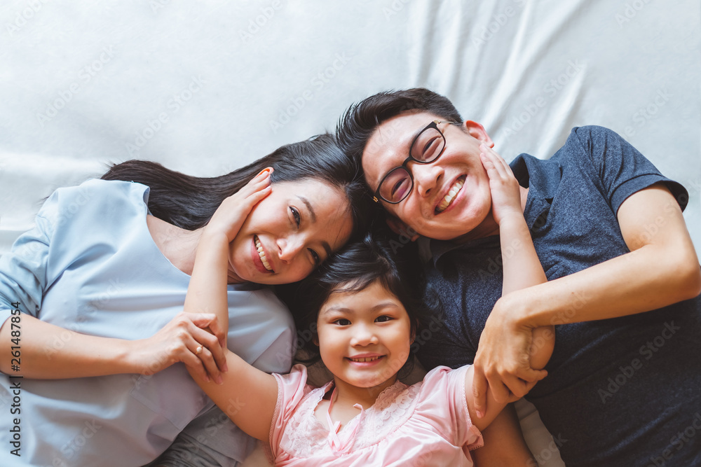 快乐的亚洲家庭躺在卧室的床上，面带微笑，俯视图